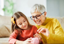 Vermögensbarometer 2024: Die finanzielle Zufriedenheit steigt wieder Großmutter und ihre Enkelin werfen Geld in ein pinkes Sparschwein.