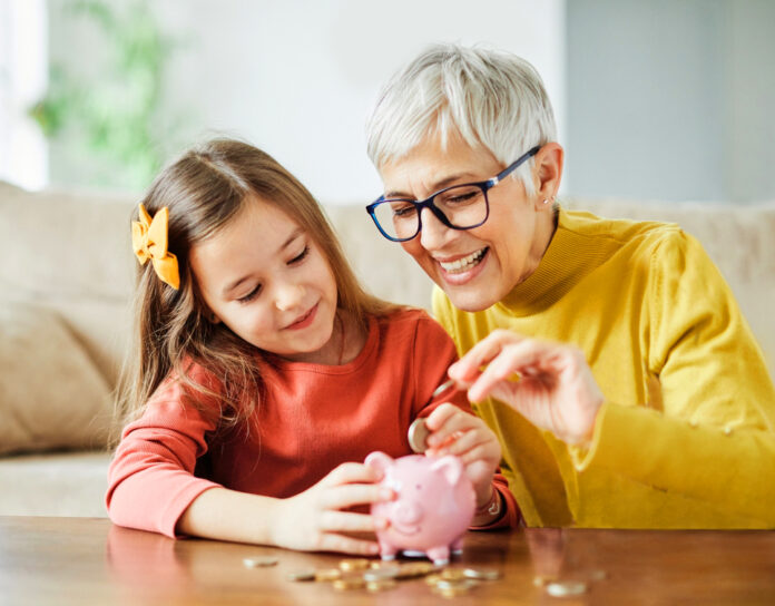 Großmutter und ihre Enkelin werfen Geld in ein pinkes Sparschwein.