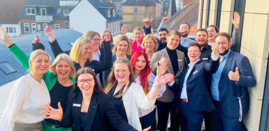 Quereinstieg bei der Förde Sparkasse Viele Frauen und Männer schauen jubelnd auf einem Gruppenbild in die Kamera.