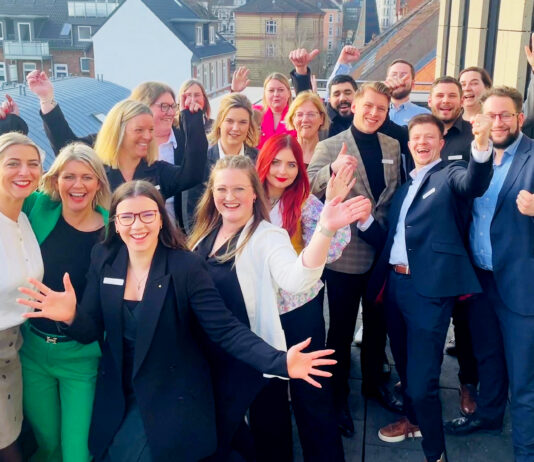Quereinstieg bei der Förde Sparkasse Viele Frauen und Männer schauen jubelnd auf einem Gruppenbild in die Kamera.