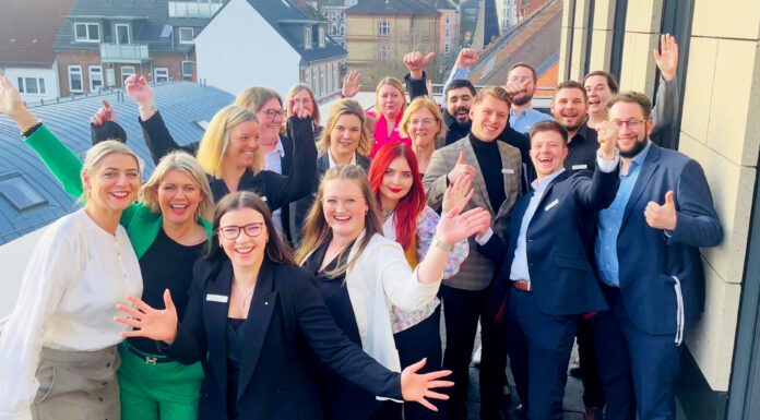 Quereinstieg bei der Förde Sparkasse Viele Frauen und Männer schauen jubelnd auf einem Gruppenbild in die Kamera.