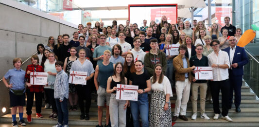 Netrace – Die Internetralley für Schüler:innen Gruppe von Schülerinnen und Schülern, die auf einer Treppe stehen und Plakate mit Gewinnsummen hochhalten.