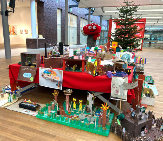 Lotties Welt: Über 90 Wünsche bei der Aktion „Wunschbaum“ Ein Fliegenpilz Maskottchen steht hinter einem Tisch voller Basteleien von Kindern, im Hintergrund ein Weihnachtsbaum
