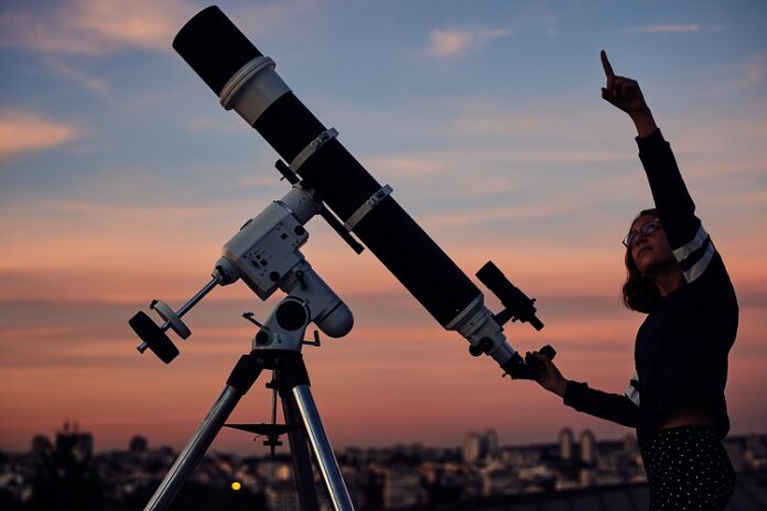 Frau zeigt in den Himmel vor einem Teleskop