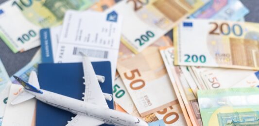 Flugpreise steigen 2025 Kleines Spielzeugflugzeuge steht auf mehreren Euro-Banknoten und einem Flugticket.