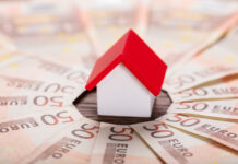 Günstiger ins Eigenheim: 10 Sparfaktoren Spielzeughaus mit rotem Dach steht im Zentrum von gefächerten 50-Euro-Scheinen.