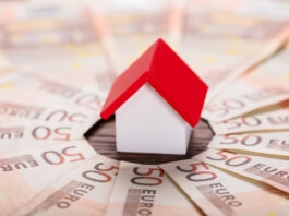 Günstiger ins Eigenheim: 10 Sparfaktoren Spielzeughaus mit rotem Dach steht im Zentrum von gefächerten 50-Euro-Scheinen.