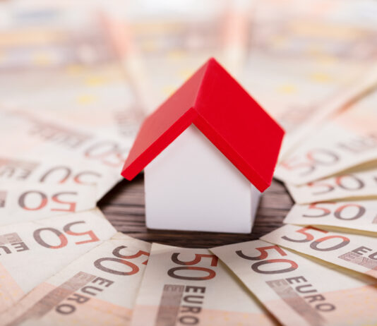 Günstiger ins Eigenheim: 10 Sparfaktoren Spielzeughaus mit rotem Dach steht im Zentrum von gefächerten 50-Euro-Scheinen.