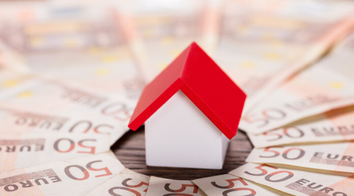 Günstiger ins Eigenheim: 10 Sparfaktoren Spielzeughaus mit rotem Dach steht im Zentrum von gefächerten 50-Euro-Scheinen.