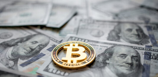 Bitcoin: Zwischen Rallye und Risiken Goldene Bitcoin Münze liegt auf mehreren 100-Dollar-Scheinen.