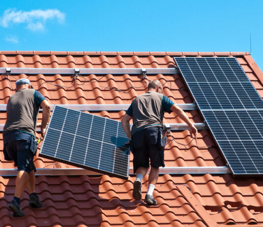 Photovoltaik: Wann sich Strom vom Dach lohnt Zwei Arbeiter installieren eine Solarzelle auf einem roten Ziegeldach.