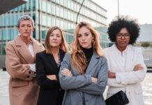 Gender Pay Gap: Darum sollten sich Frauen früh für ein gutes Gehalt stark machen Vier Geschäftsfrauen verschiedenen Alters und verschiedener Herkunft stehen mit verschränkten Armen nebeneinander und schauen entschlossen nach vorn.