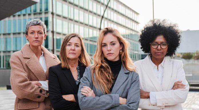 Gender Pay Gap: Darum sollten sich Frauen früh für ein gutes Gehalt stark machen Vier Geschäftsfrauen verschiedenen Alters und verschiedener Herkunft stehen mit verschränkten Armen nebeneinander und schauen entschlossen nach vorn.