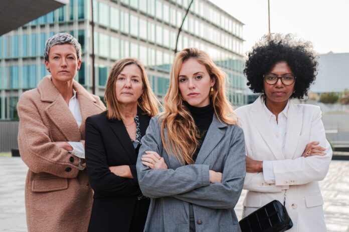 Vier Geschäftsfrauen verschiedenen Alters und verschiedener Herkunft stehen mit verschränkten Armen nebeneinander und schauen entschlossen nach vorn.