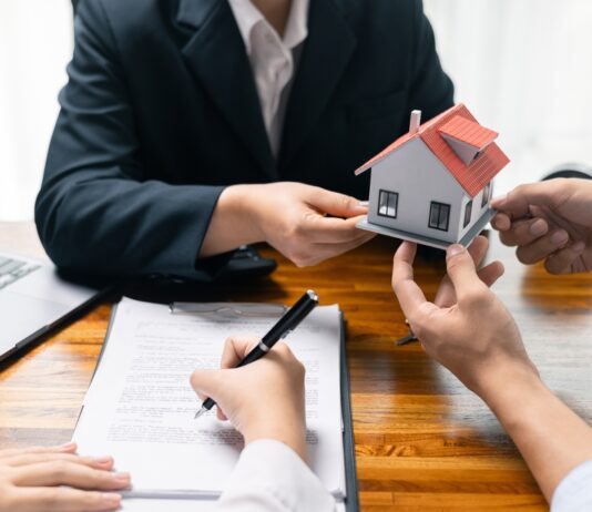 Maklervertrag für Kaufinteressierte: Was bedeutet das genau? Immobilienmakler überreicht ein Modell eines Einfamilienhauses, parallel wird ein Vertrag unterschrieben
