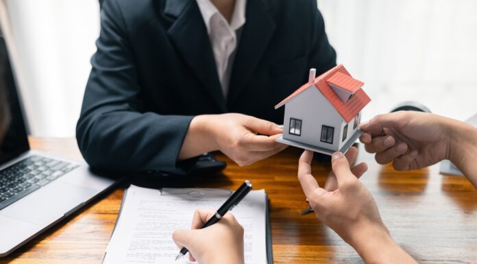 Maklervertrag für Kaufinteressierte: Was bedeutet das genau? Immobilienmakler überreicht ein Modell eines Einfamilienhauses, parallel wird ein Vertrag unterschrieben