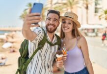 So machen die Deutschen Urlaub Touristenpaar von Mann und Frau machen ein Selfie von sich, wie sie Eis in der Waffel am Meer essen