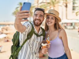 So machen die Deutschen Urlaub Touristenpaar von Mann und Frau machen ein Selfie von sich, wie sie Eis in der Waffel am Meer essen