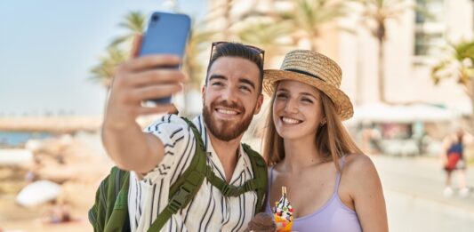 So machen die Deutschen Urlaub Touristenpaar von Mann und Frau machen ein Selfie von sich, wie sie Eis in der Waffel am Meer essen