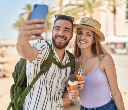 So machen die Deutschen Urlaub Touristenpaar von Mann und Frau machen ein Selfie von sich, wie sie Eis in der Waffel am Meer essen