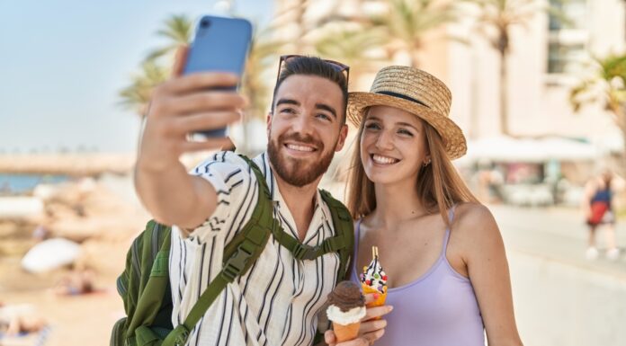 So machen die Deutschen Urlaub Touristenpaar von Mann und Frau machen ein Selfie von sich, wie sie Eis in der Waffel am Meer essen