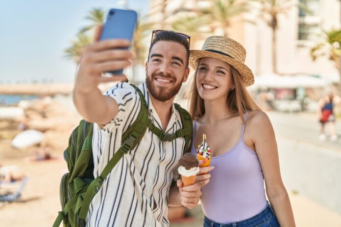Touristenpaar von Mann und Frau machen ein Selfie von sich, wie sie Eis in der Waffel am Meer essen