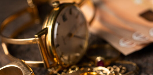 So viel Geld bekommen Sie für alten Schmuck Eine alte Uhr und Ketten und Ringe aus Gold liegen auf einem Haufen, im Hintergrund sind 50-Euro-Scheine zu sehen