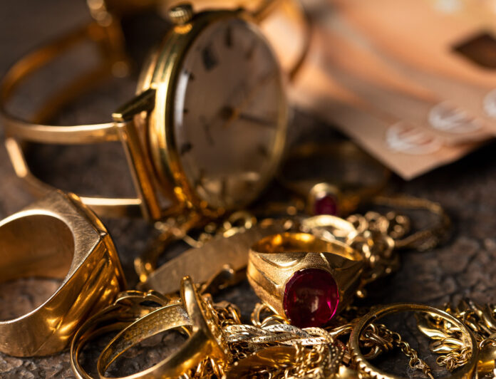 Eine alte Uhr und Ketten und Ringe aus Gold liegen auf einem Haufen, im Hintergrund sind 50-Euro-Scheine zu sehen
