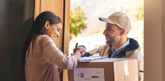 Paket kaputt, verschwunden oder bei Nachbar:innen – Wer haftet wann? Eine Frau nimmt vom Paketboten ein Paket an und unterschreibt dafür.
