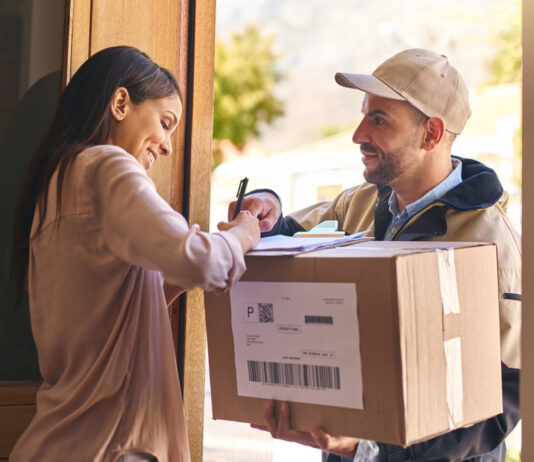 Paket kaputt, verschwunden oder bei Nachbar:innen – Wer haftet wann? Eine Frau nimmt vom Paketboten ein Paket an und unterschreibt dafür.