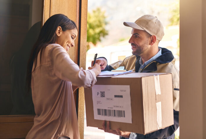 Eine Frau nimmt vom Paketboten ein Paket an und unterschreibt dafür.