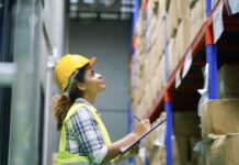 Supply-Chain-Management: Lieferketten krisensicher aufstellen Eine Frau mit Sicherheitsweste und Bauhelm überprüft den Lagerbestand mit einem Klemmbrett