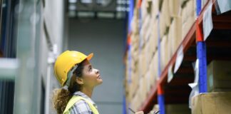 Supply-Chain-Management: Lieferketten krisensicher aufstellen Eine Frau mit Sicherheitsweste und Bauhelm überprüft den Lagerbestand mit einem Klemmbrett