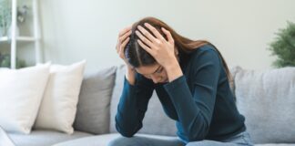 Schulden schnell abbauen: Tipps & Tricks Frau sitzt zuhause auf dem Sofa und stützt verzweifelt den Kopf in die Hände. Vor ihr auf dem Tisch stehen ein aufgeklapptes MacBook, Kreditkarte, Notizblock und Taschenrechner.