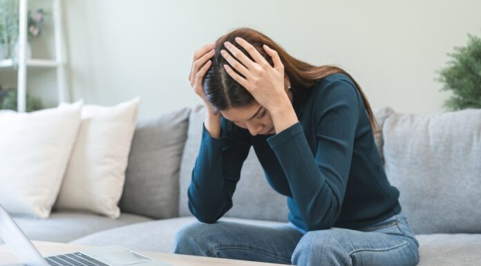 Schulden schnell abbauen: Tipps & Tricks Frau sitzt zuhause auf dem Sofa und stützt verzweifelt den Kopf in die Hände. Vor ihr auf dem Tisch stehen ein aufgeklapptes MacBook, Kreditkarte, Notizblock und Taschenrechner.