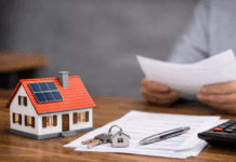 Eigenheim und Miete 2026: Neue Rechte, neue Plichten, neue Chancen Modell eines Einfamilienhauses mit Solarpanel auf dem Dach, daneben Hausschlüssel, Vertragsunterlagen, Stift und Taschenrechner auf einem Holztisch.