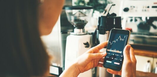 Rekord: 14 Millionen investierten 2025 in Aktienanlagen Frau schaut auf Handy mit Aktienkurs auf dem Display