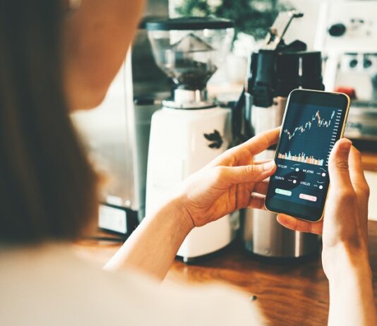 Rekord: 14 Millionen investierten 2025 in Aktienanlagen Frau schaut auf Handy mit Aktienkurs auf dem Display