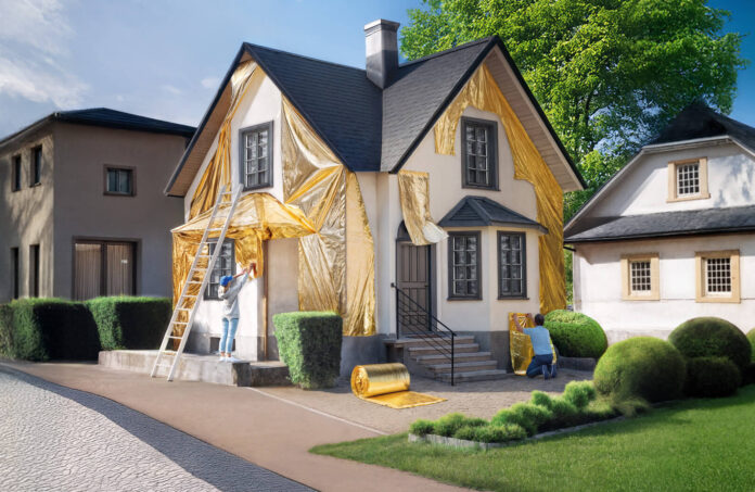 Ein weißes Einfamilienhaus wird von einer Frau und einem Mann mit goldener Folie verkleidet. Vorn am Haus lehnt eine weiße Leiter.