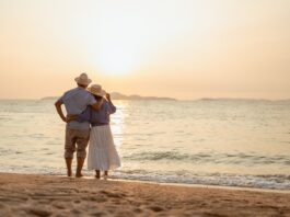 Rente im Ausland: Was Sie alles wissen sollten Ein Paar, das bei Sonnenuntergang am Strand steht, wobei der Mann die Hand der Frau hält.