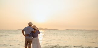 Rente im Ausland: Was Sie alles wissen sollten Ein Paar, das bei Sonnenuntergang am Strand steht, wobei der Mann die Hand der Frau hält.