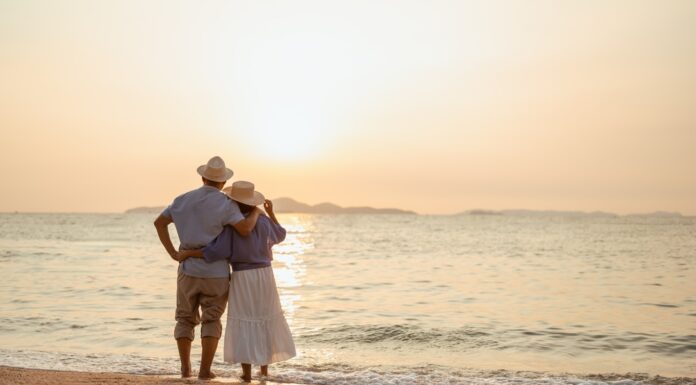 Rente im Ausland: Was Sie alles wissen sollten Ein Paar, das bei Sonnenuntergang am Strand steht, wobei der Mann die Hand der Frau hält.