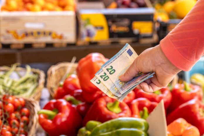 Gemüse im Supermarkt. davor wird eine Hand gehalten, in der sich zwei 20-Euro-Scheine und ein 5-Euro-Schein befinden.