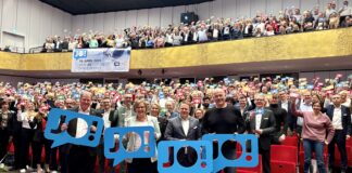 Wir sagen „JO!“ zu den Olympischen Spielen in Kiel Viele Menschen stehen im Konzertsaal des Kieler Schlosses und halten bunte Schilder hoch, auf denen "JO!" steht.