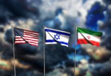 Iran-Krieg: Das wird nun teurer Die Flaggen von den USA, Isreal und Iran wehen vor einem dunklen, wolkenverhangenen Himmel.