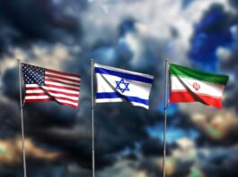 Iran-Krieg: Das wird nun teurer Die Flaggen von den USA, Isreal und Iran wehen vor einem dunklen, wolkenverhangenen Himmel.