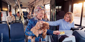 Bargeldlos zahlen in KVG-Bussen Eine ältere Dame hat zwei Hunde auf dem Arm und bezahlt in einem Bus mit ihrer Kreditkarte. Die Busfahrerin lächelt und streichelt die Hunde.