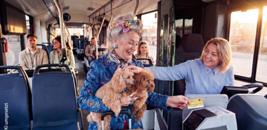 Bargeldlos zahlen in KVG-Bussen Eine ältere Dame hat zwei Hunde auf dem Arm und bezahlt in einem Bus mit ihrer Kreditkarte. Die Busfahrerin lächelt und streichelt die Hunde.