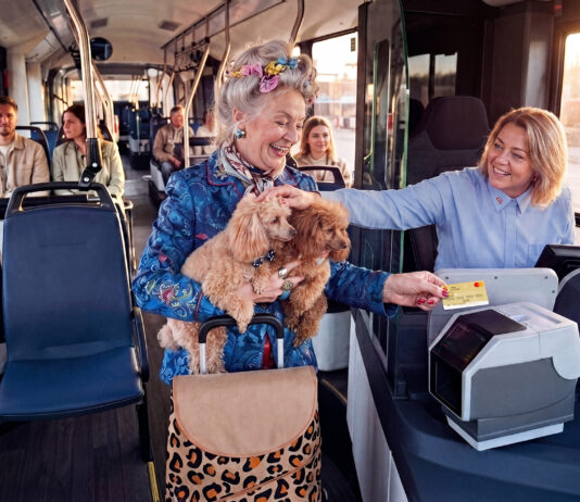 Bargeldlos zahlen in KVG-Bussen Eine ältere Dame hat zwei Hunde auf dem Arm und bezahlt in einem Bus mit ihrer Kreditkarte. Die Busfahrerin lächelt und streichelt die Hunde.