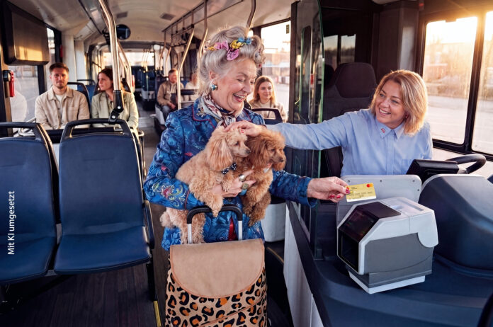 Eine ältere Dame hat zwei Hunde auf dem Arm und bezahlt in einem Bus mit ihrer Kreditkarte. Die Busfahrerin lächelt und streichelt die Hunde.